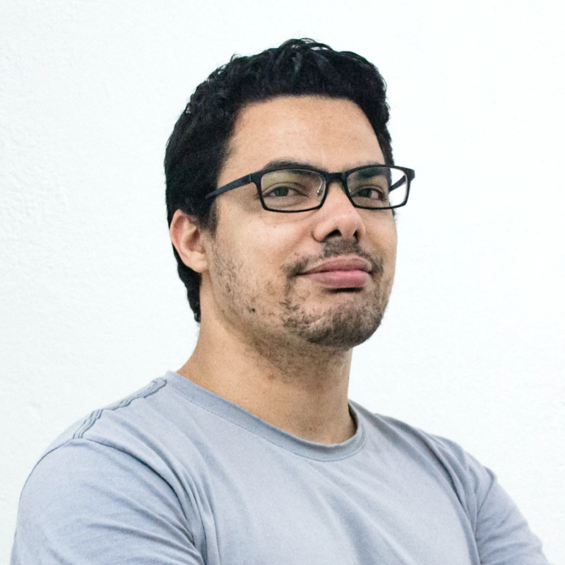 Confident young man in a white shirt posing thoughtfully against a pink background.