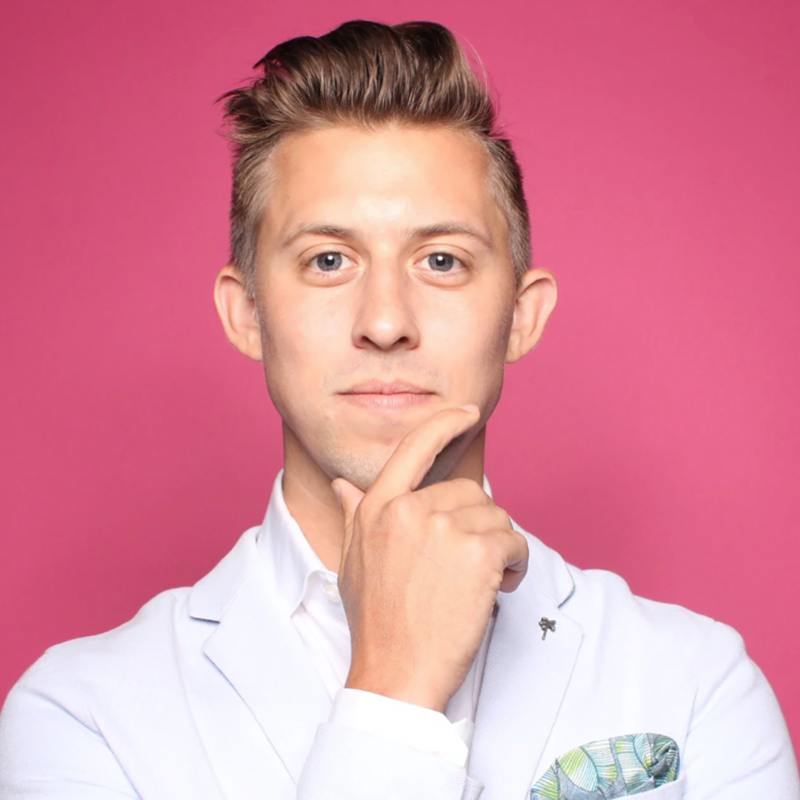 Confident young man in a white shirt posing thoughtfully against a pink background.