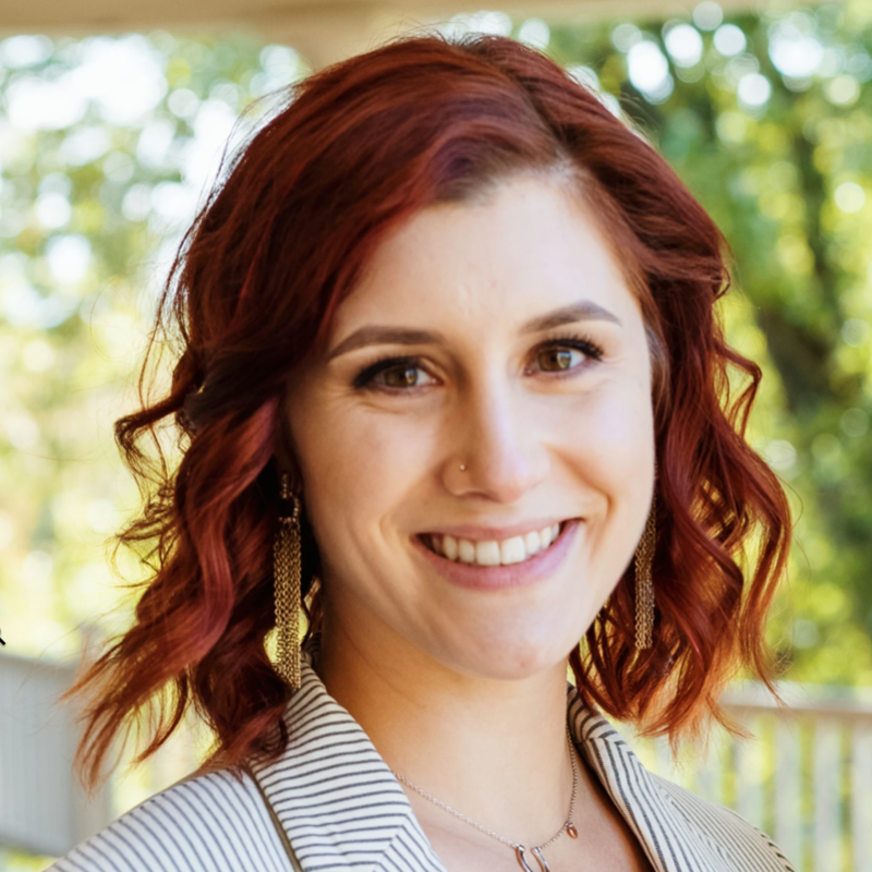 Smiling woman with red hair and a light blazer outdoors.