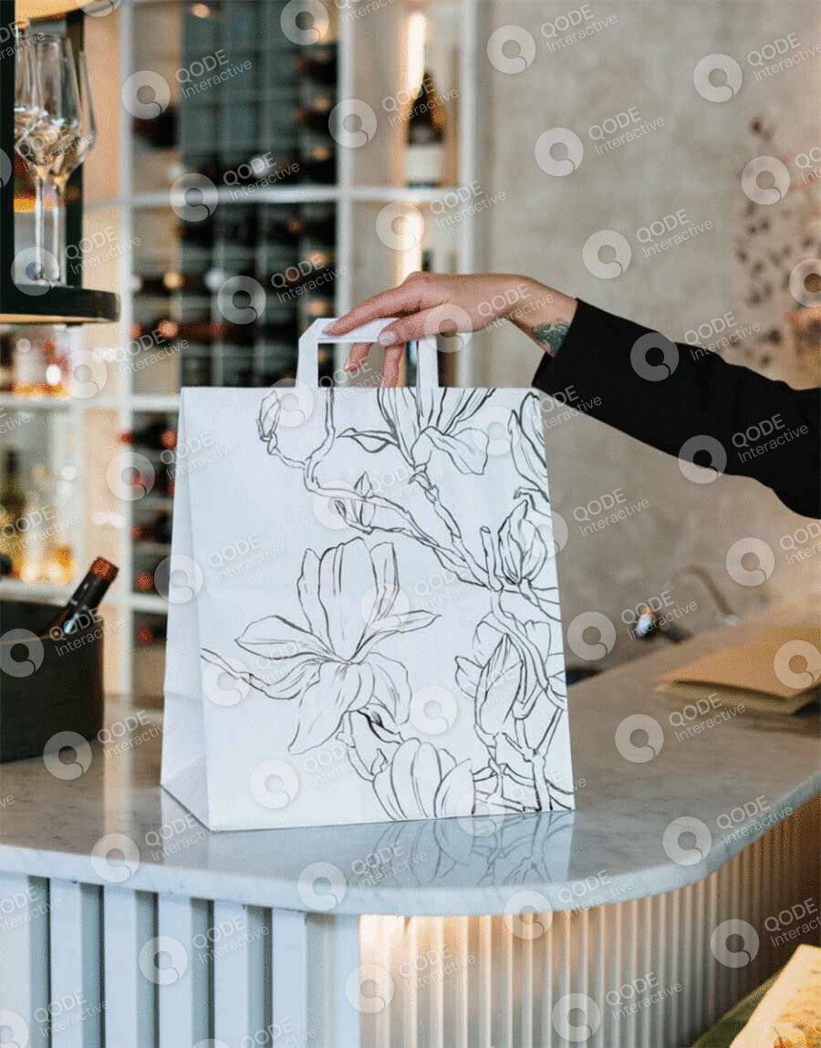Hand holding a floral-designed white paper bag in a modern cafe.