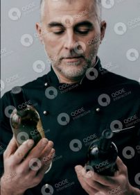 A chef examining two bottles of sauces or oils in a kitchen setting.