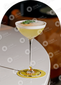 A frothy cocktail garnished with herbs in a coupe glass.