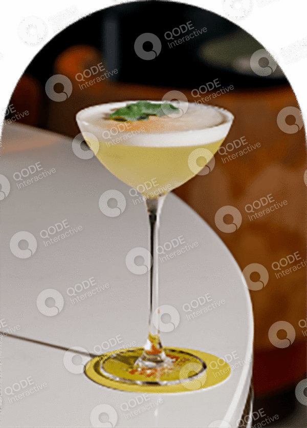 A frothy cocktail garnished with herbs in a coupe glass.