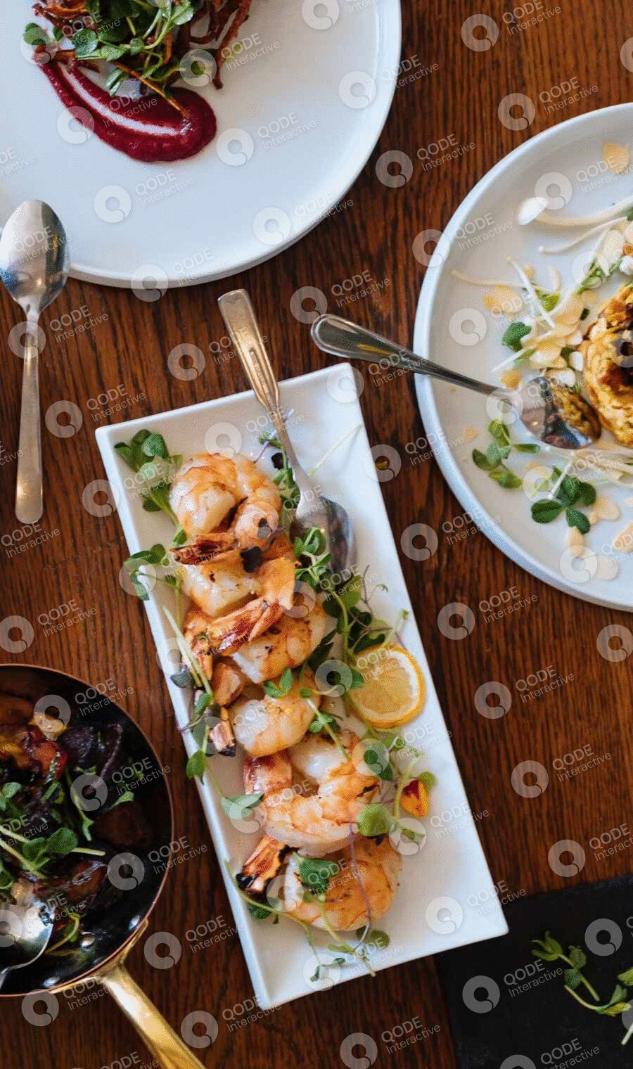 Grilled shrimp served on a rectangular white dish with lemon slices and herbs.