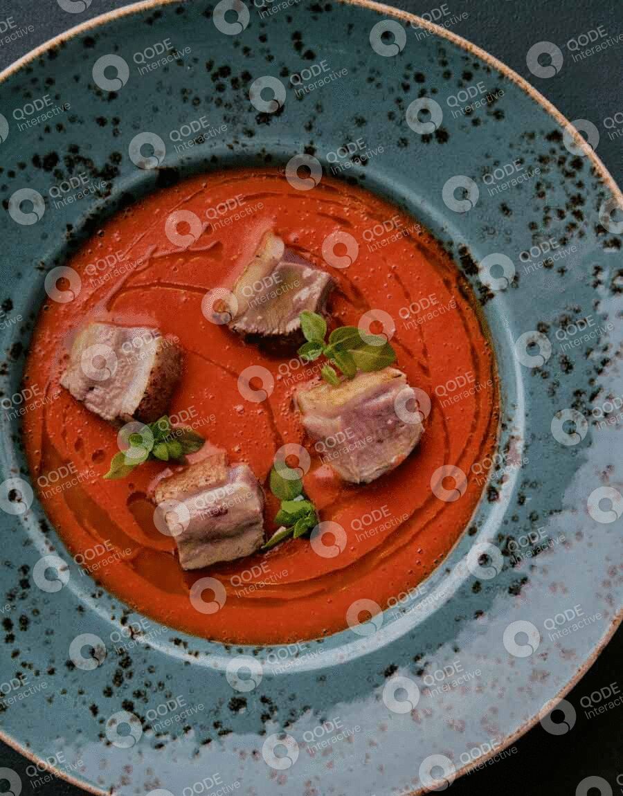 Gourmet dish with sliced meat on vibrant red sauce, garnished with green herbs.
