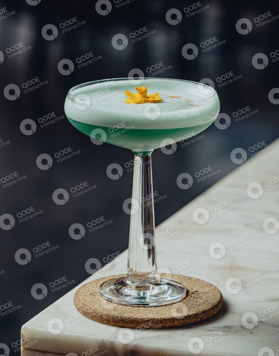 Green cocktail with a flower garnish in a coupe glass.