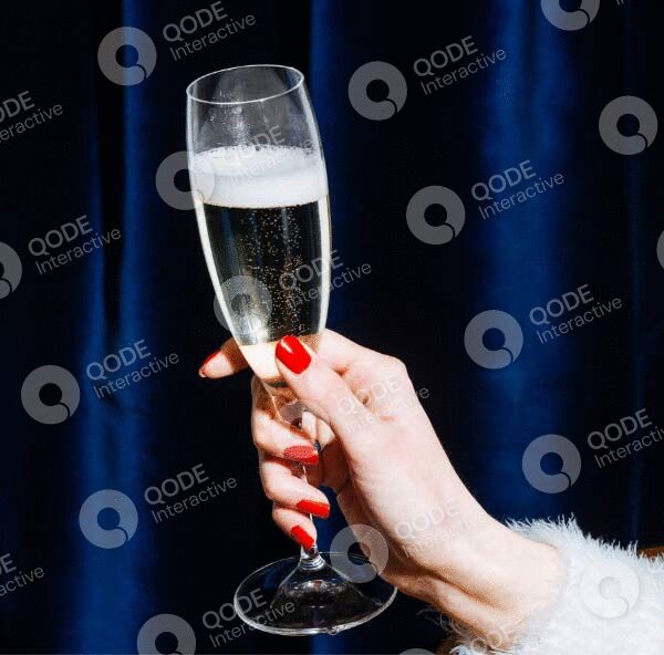 Hand holding a champagne flute with sparkling wine against a dark background.