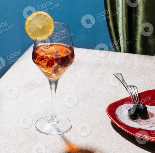 Elegant cocktail with lemon garnish on white table beside cactus.