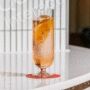 A tall glass with an orange slice and ice on a white surface.