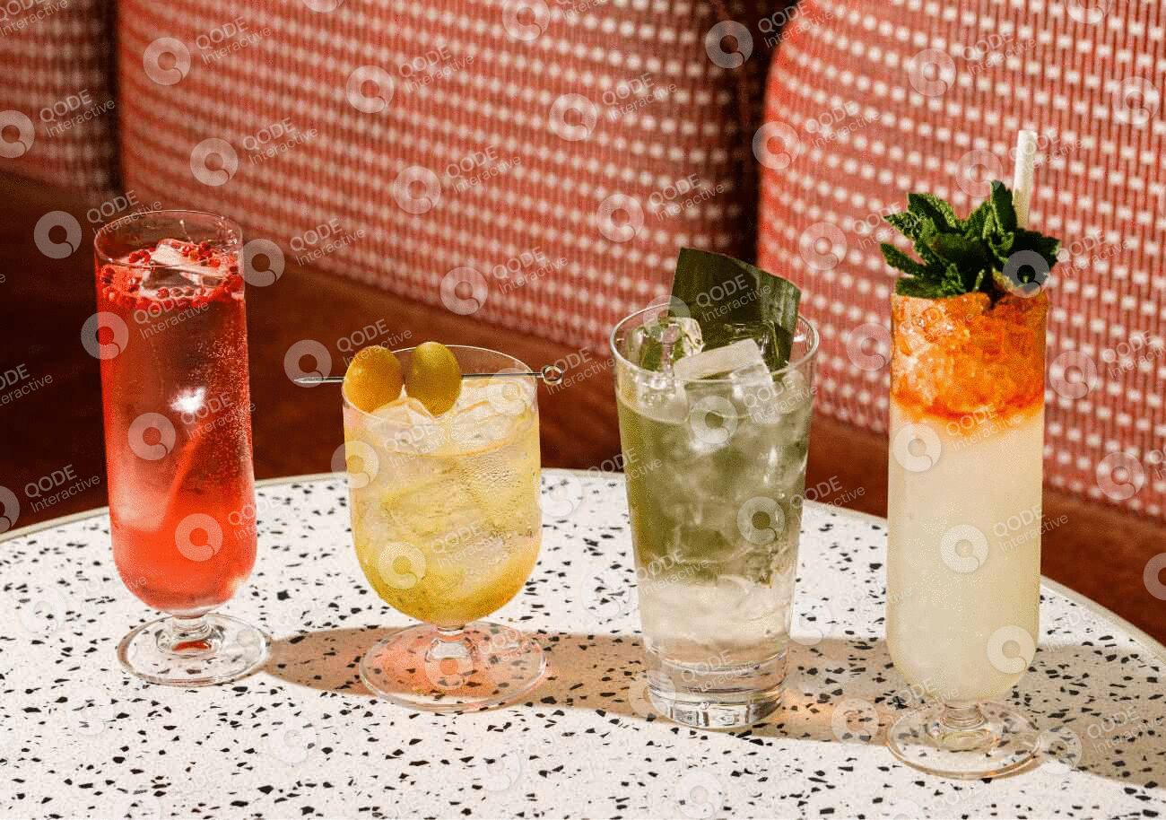 A row of four colorful cocktails with fresh garnishes on a terrazzo table.