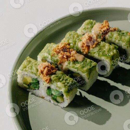 Delicious sushi rolls topped with green avocado and crispy tempura flakes on a green ceramic plate.