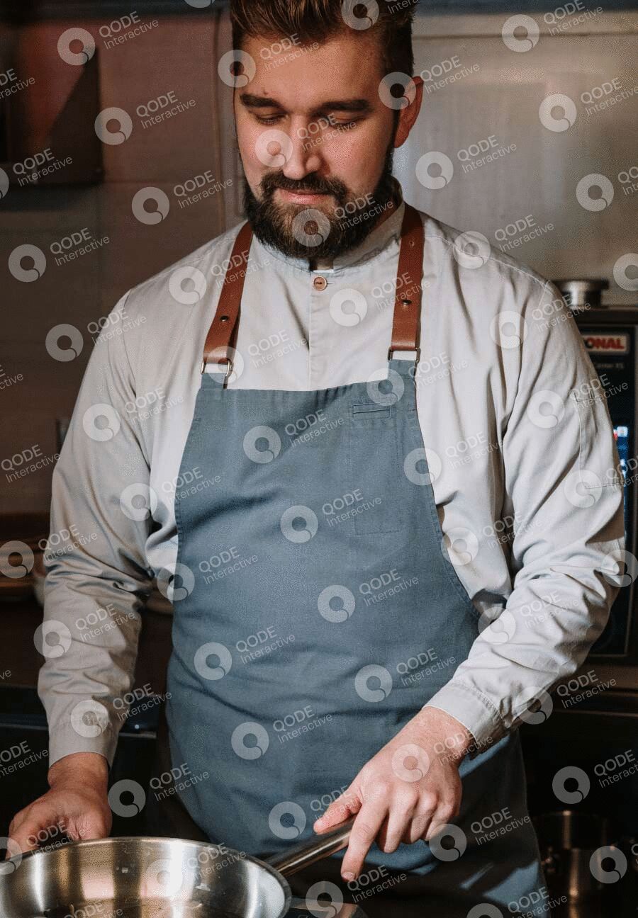 Chef in a white shirt and blue apron with leather straps preparing food.