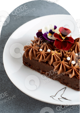 A slice of rich chocolate cake decorated with flowers and chocolate chips.