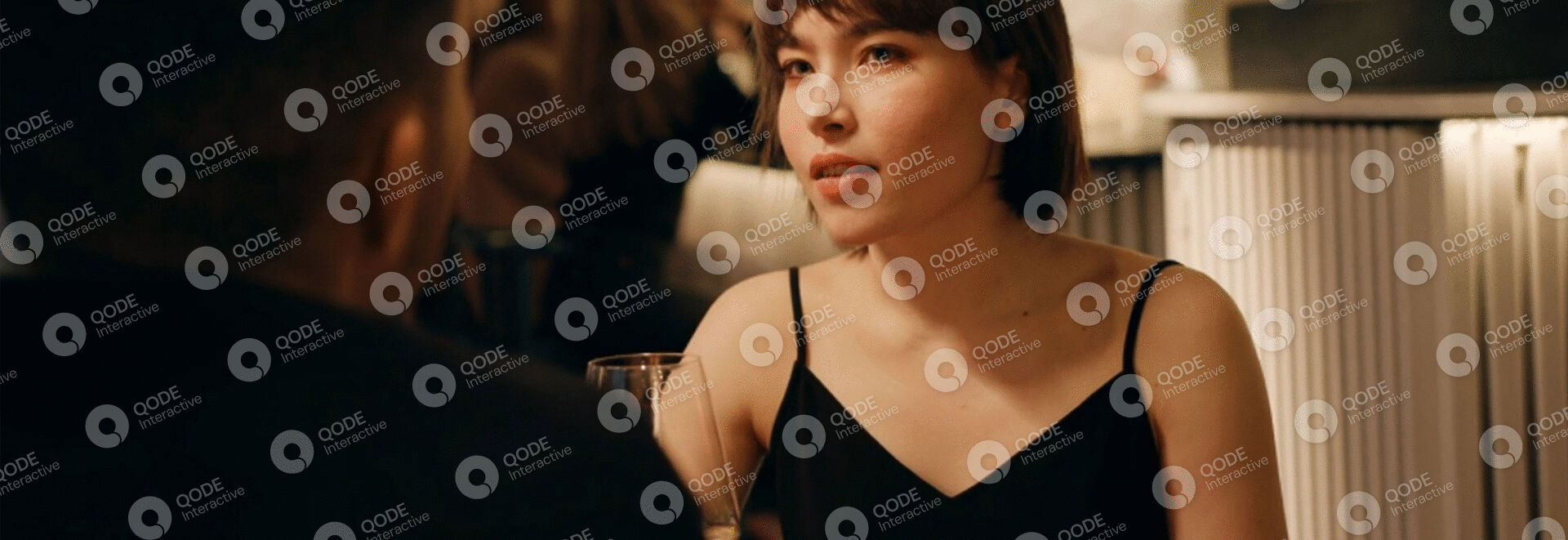 Young woman with curly hair in a black top looking thoughtfully.