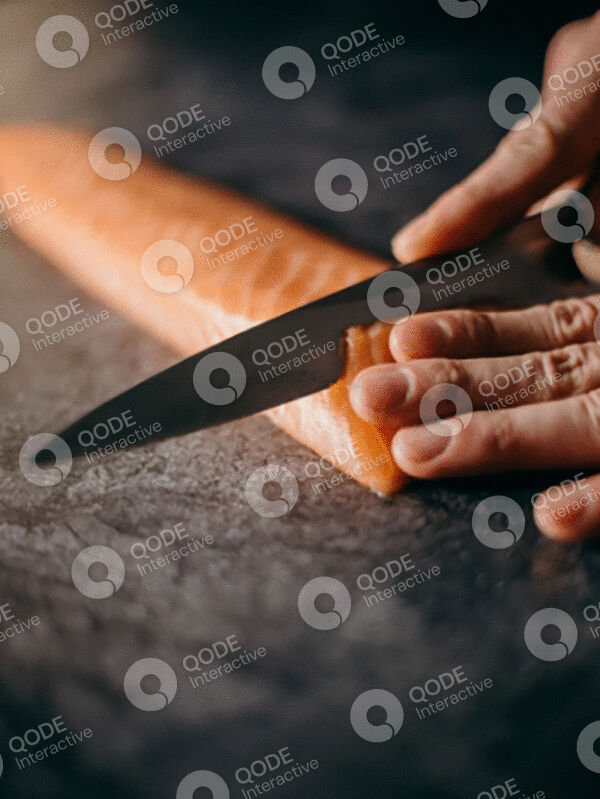 Hands slicing a fresh carrot with a knife on a cutting board.