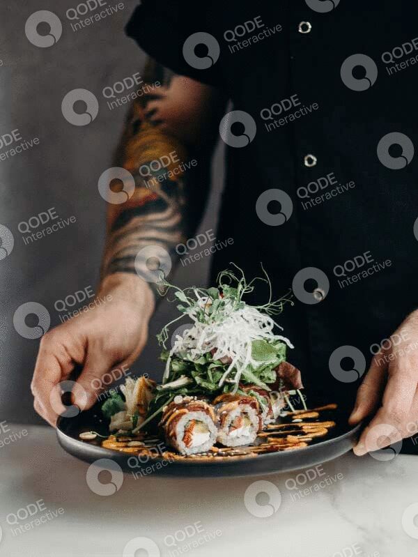 Chef presenting a beautifully plated sushi roll with garnishes.