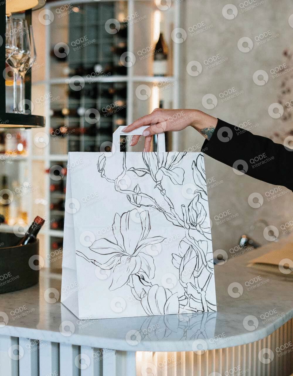 Hand placing a floral-patterned paper bag on a counter in a stylish setting.