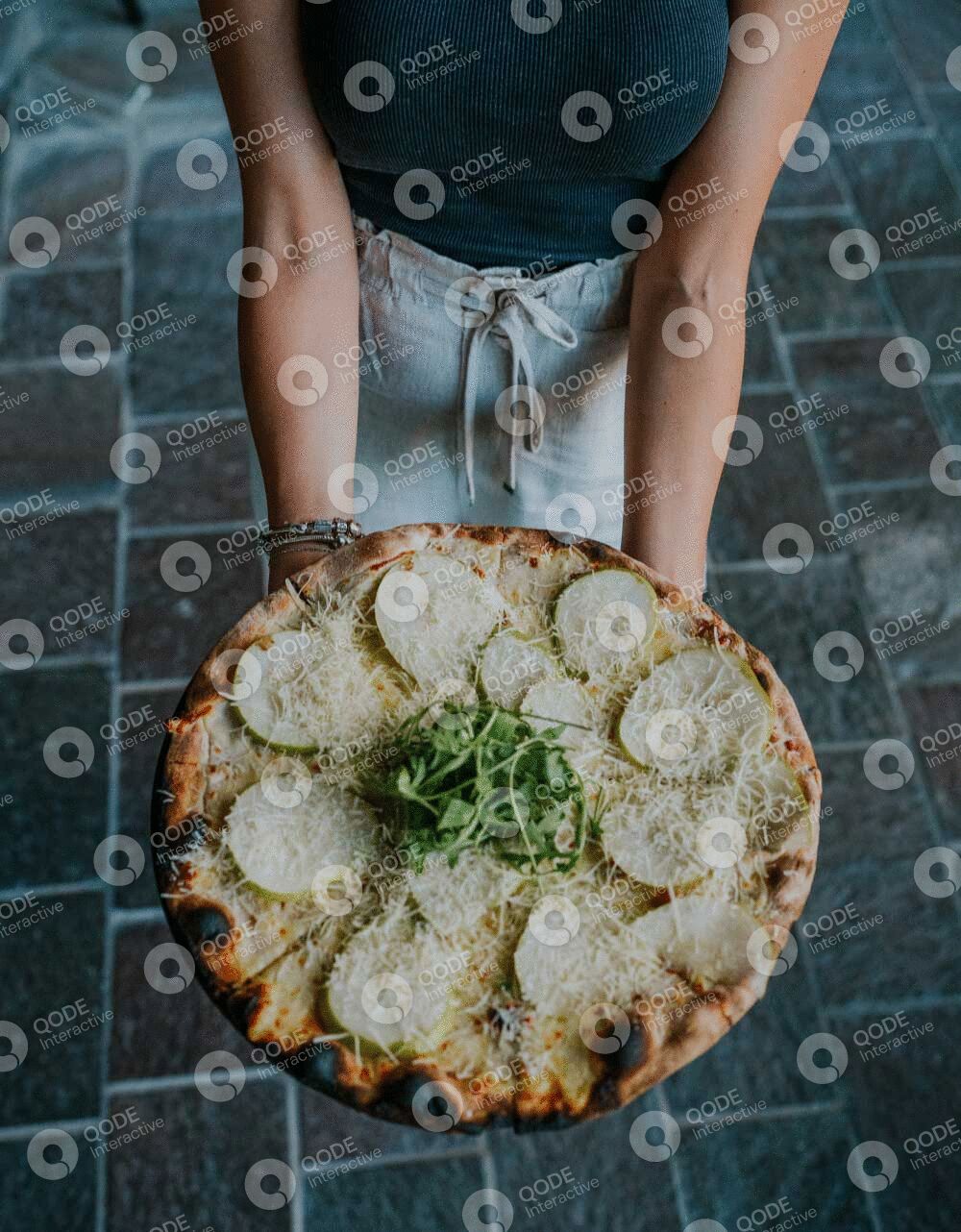 Person holding a delicious pizza topped with cheese and greens.