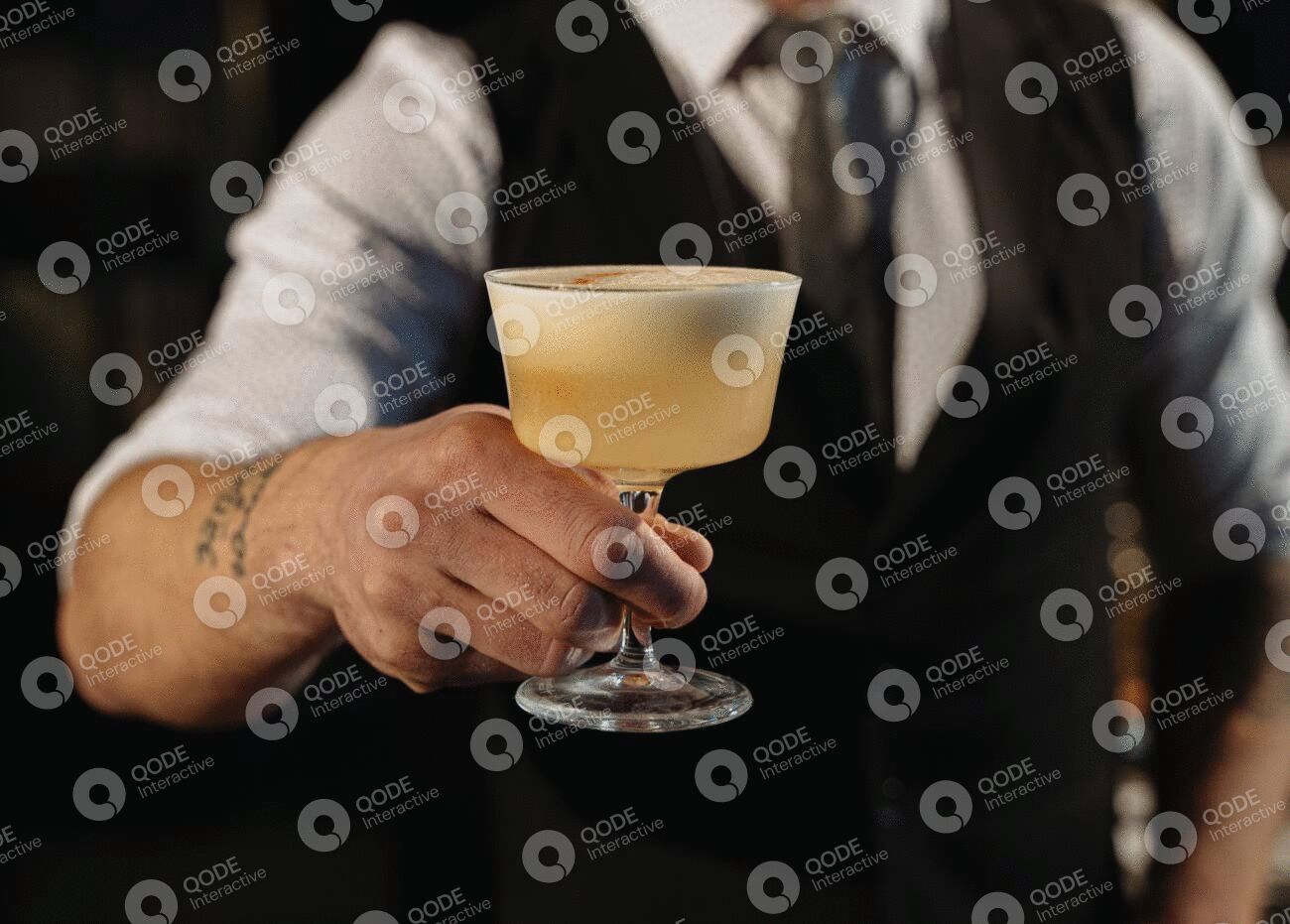 Bartender holding a frothy cocktail in a coupe glass.