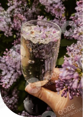 A hand holding a glass of sparkling drink with lilac flowers inside.
