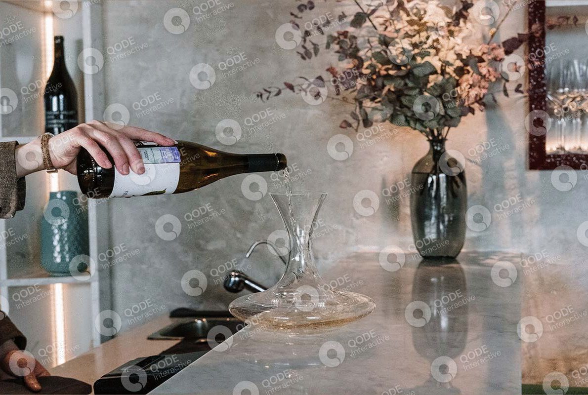 A hand pours rosé wine into a glass on a kitchen counter with flowers nearby.