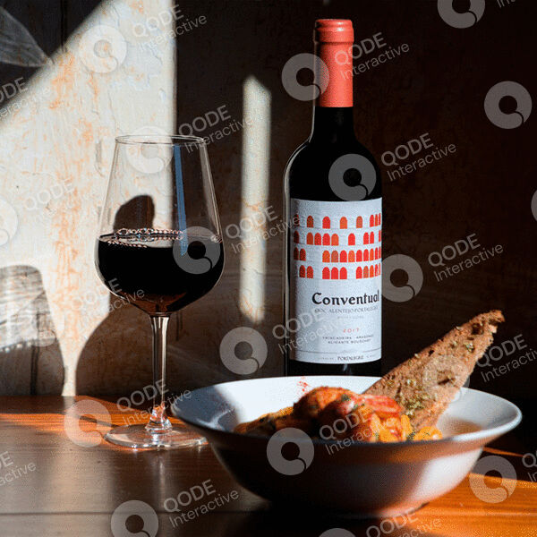 A glass of red wine and a bottle next to a bowl of breadsticks on a wooden table.