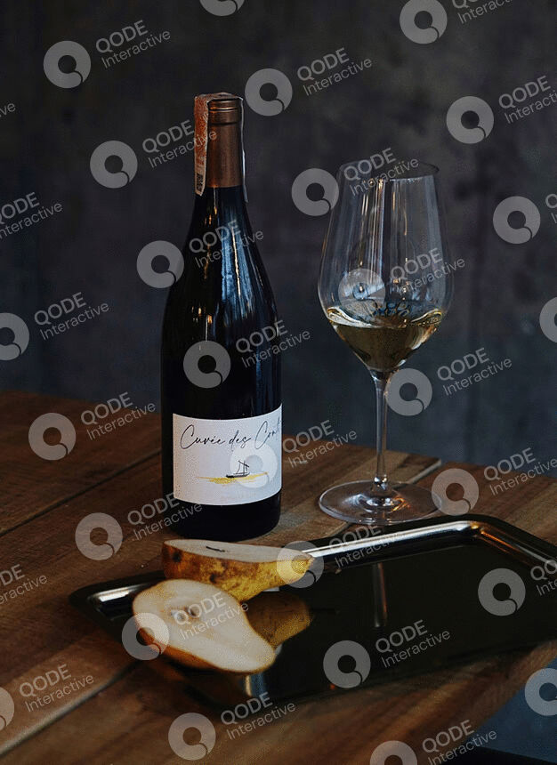 A bottle of white wine with a glass and some bread on a wooden table.