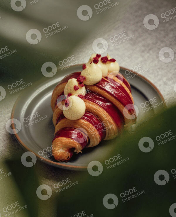 A croissant topped with creamy dollops and red syrup on a plate.