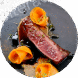 Seared steak with carrot ribbons and herbs on a dark plate.