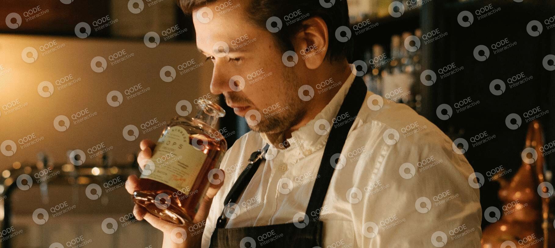 A man in an apron examining a bottle of liquor closely.