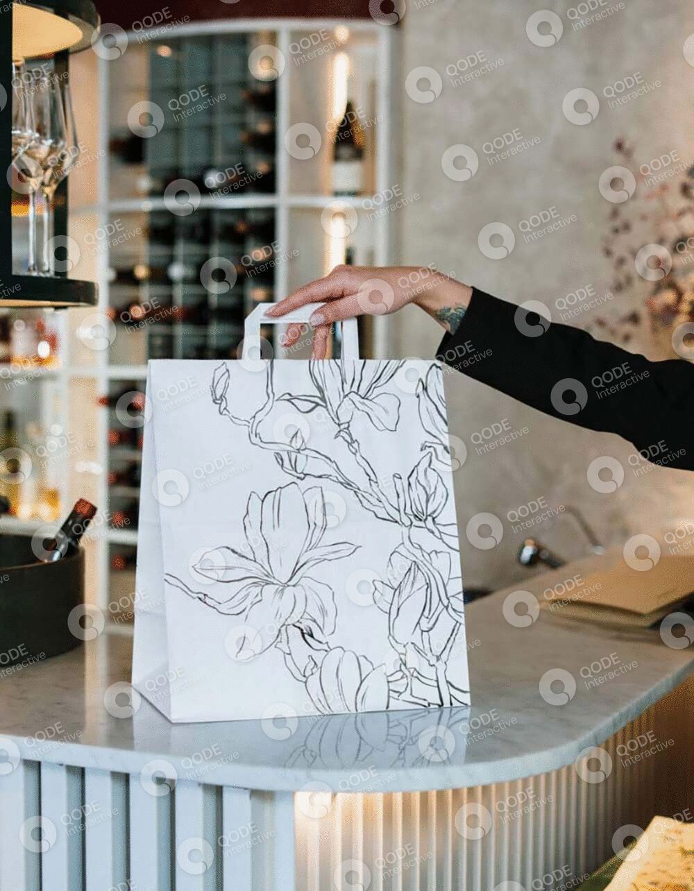 Hand holding a floral-designed white paper bag in a stylish interior.