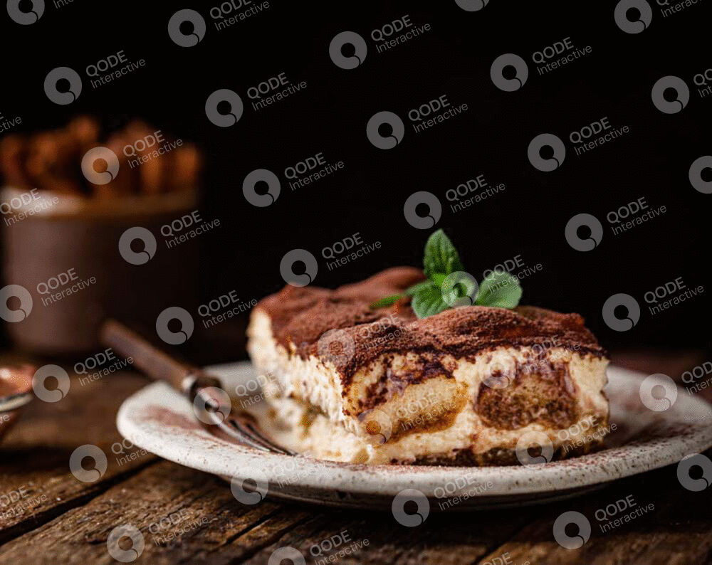 A slice of creamy tiramisu on a white plate with mint garnish.