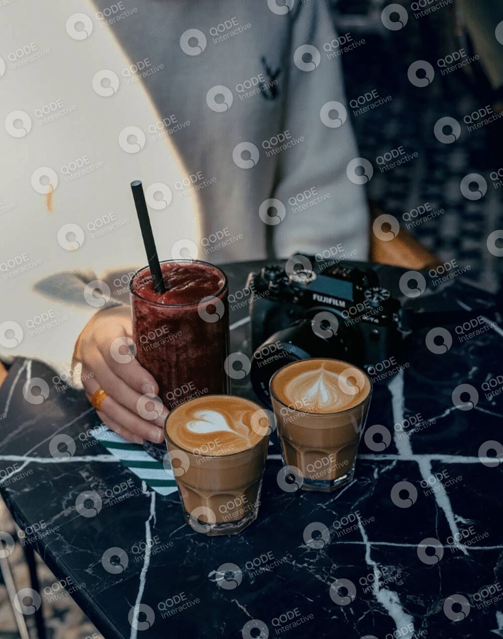 Two lattes and a smoothie on a patterned table with a person in the background.