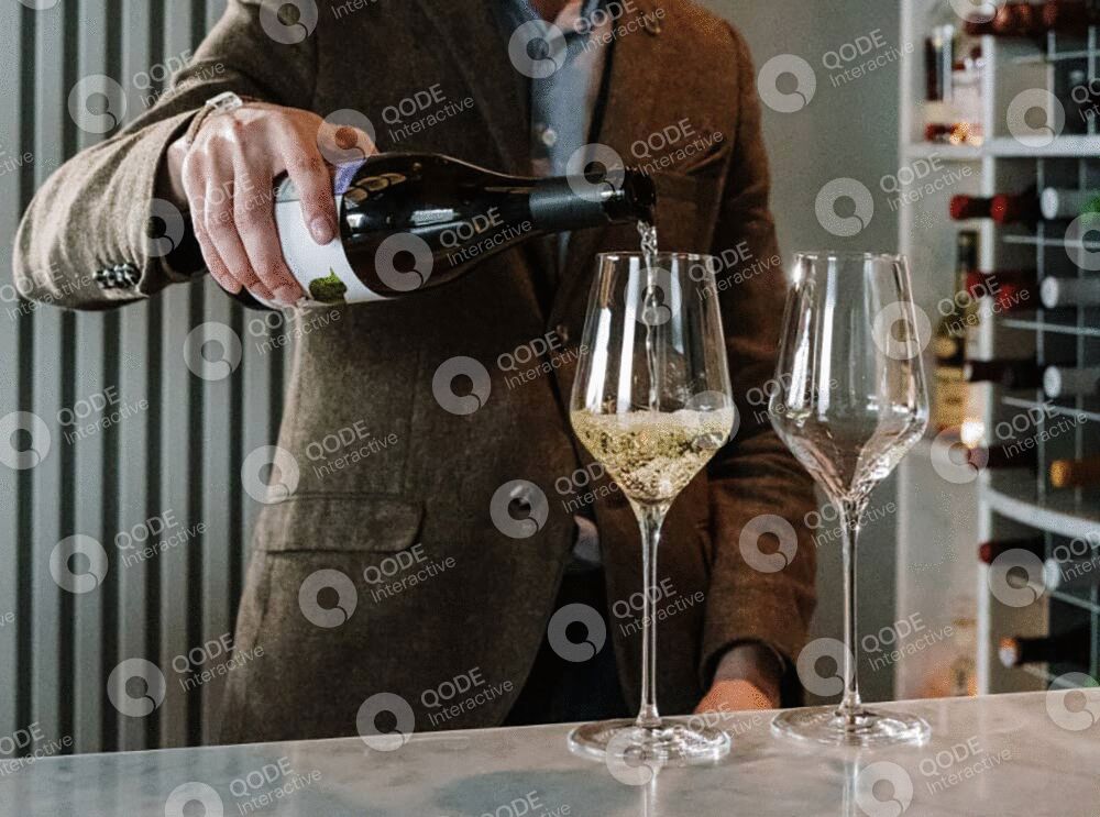 A person pours white wine into a glass, wearing a brown apron.