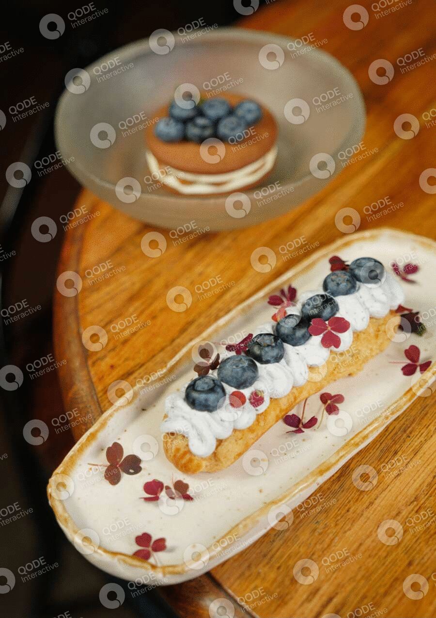 Elegant dessert with white icing, blueberries, and red garnish on a wooden table.