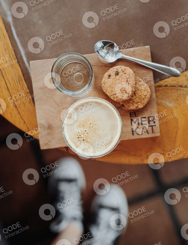 A cup of coffee with cookies and a spoon on a wooden table.