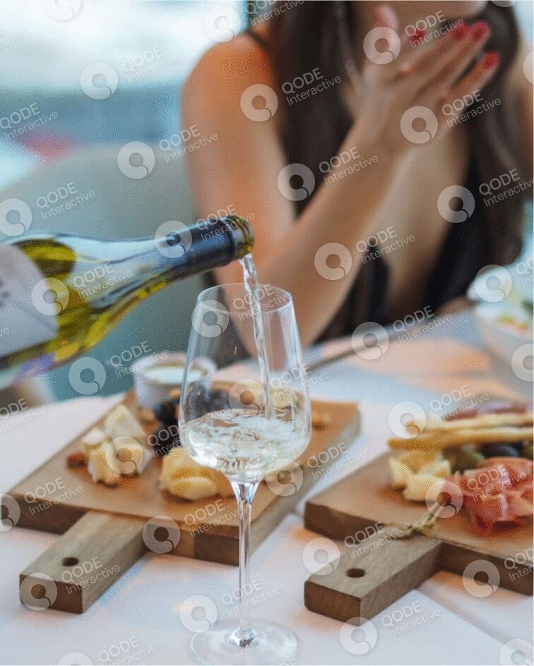 Wine being poured into a glass on a wooden board with snacks and a blurred background.