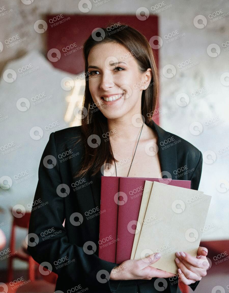 Smiling woman holding notebooks and wearing a black blazer.