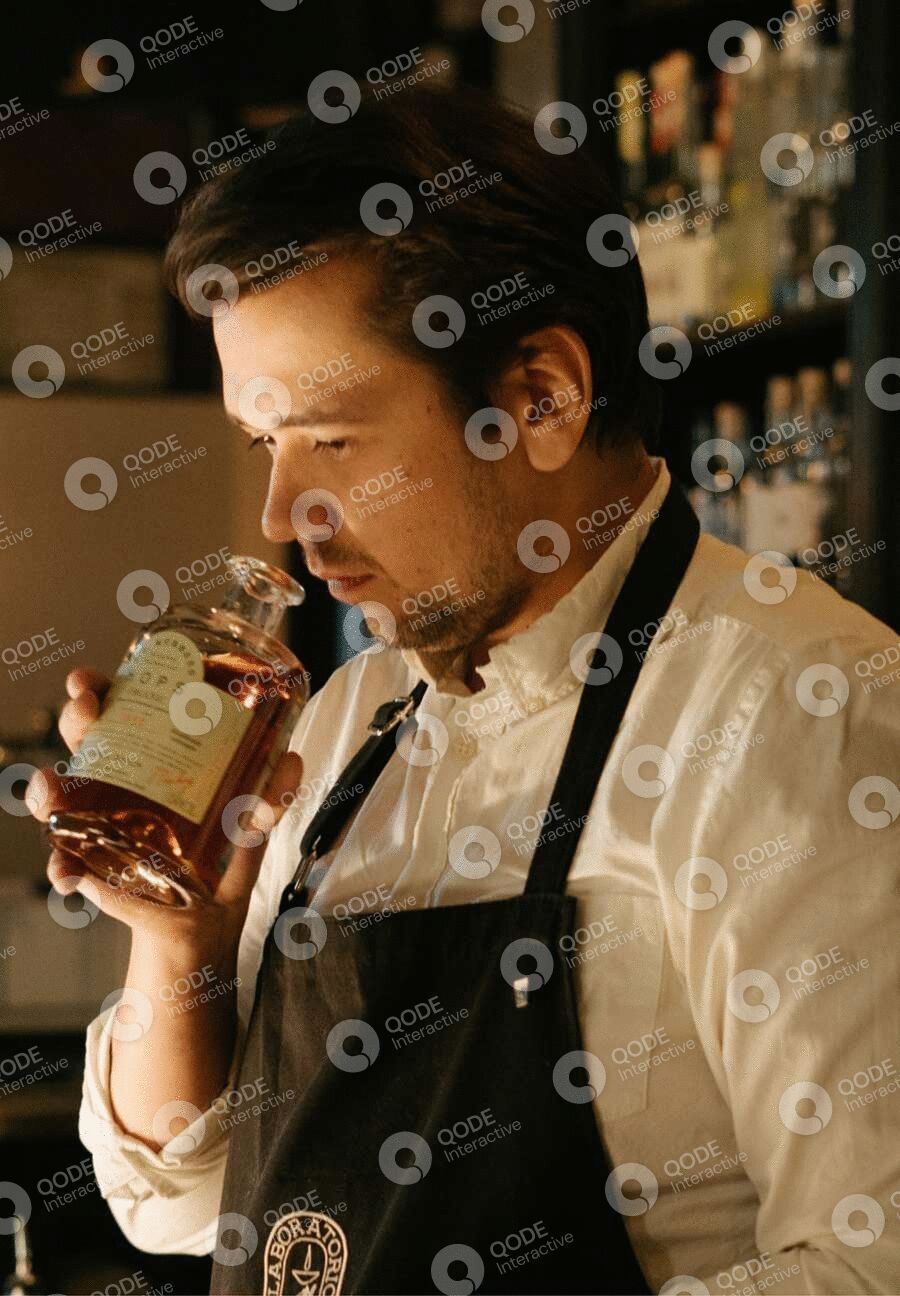 Man in apron smelling a glass of whiskey in a dimly lit room.