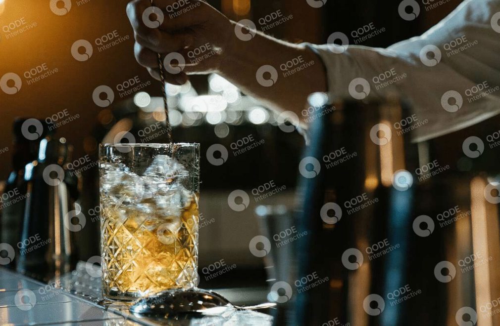 A glass of whiskey with ice cubes on a table at a bar.